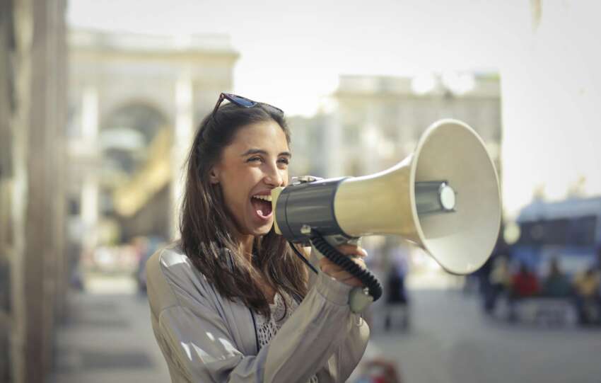 Cheerful young woman screaming into megaphone