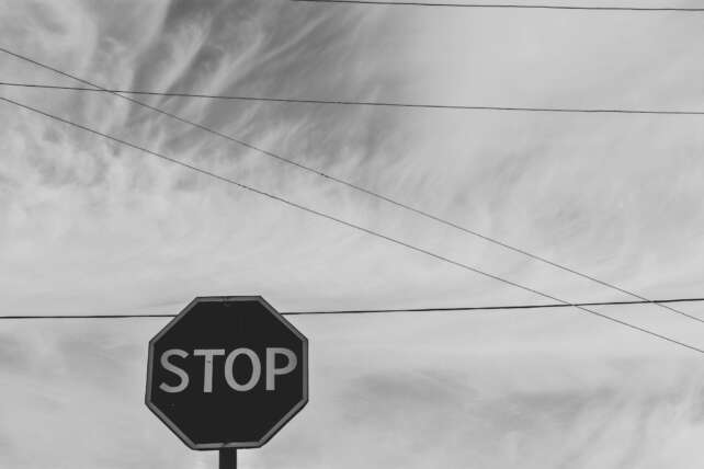 Black and white photo of a stop sign against a cloudy sky with intersecting wires.