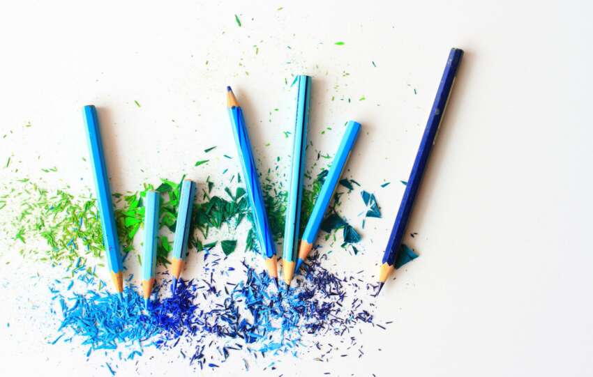 Creative display of colored pencils and vibrant shavings on a white background.