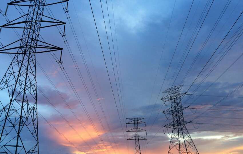 A scenic view of high voltage power lines silhouetted against a vibrant sunset sky.