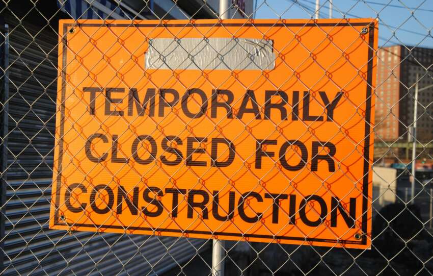 Orange sign behind fence reading 'Temporarily Closed for Construction' at site.