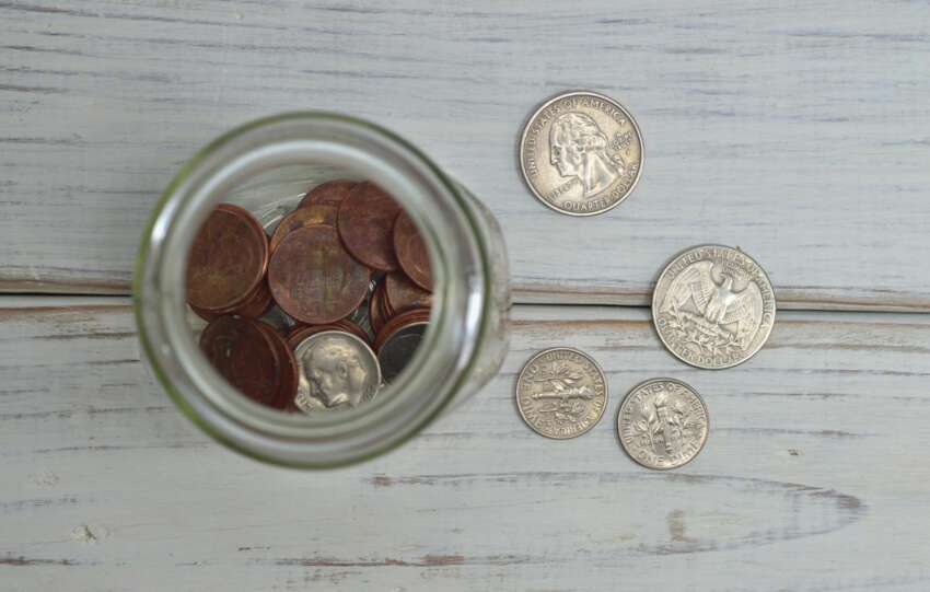 Top view of a jar filled with coins placed on a wooden table, depicting savings.