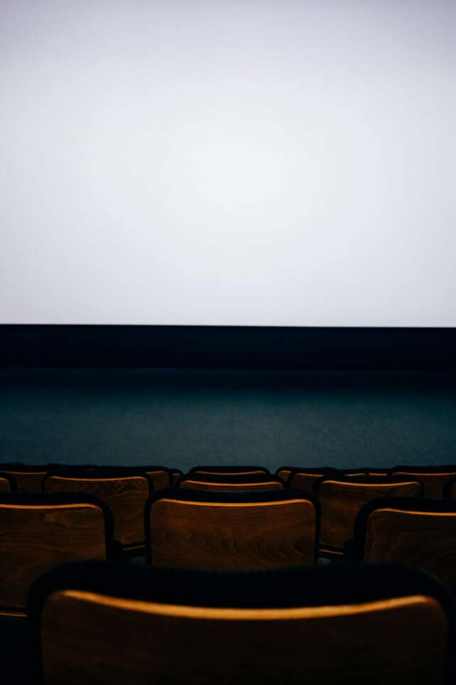 A modern, empty cinema auditorium with rows of wooden seats and a large blank screen.