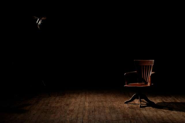 A vintage wooden chair is spotlighted in a dark studio setting, casting shadows.