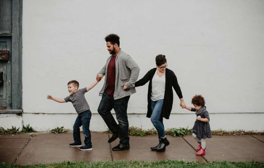 A joyful family walking together outdoors, holding hands in a playful and happy moment.