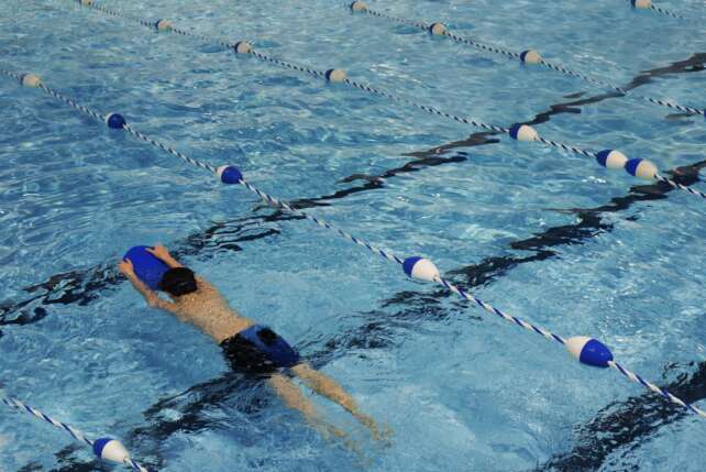 A young swimmer practicing with a kickboard in a swimming pool on a sunny day.