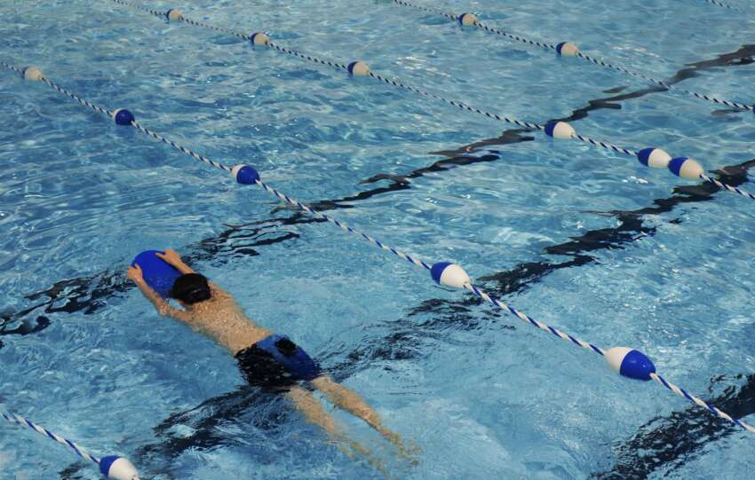 A young swimmer practicing with a kickboard in a swimming pool on a sunny day.