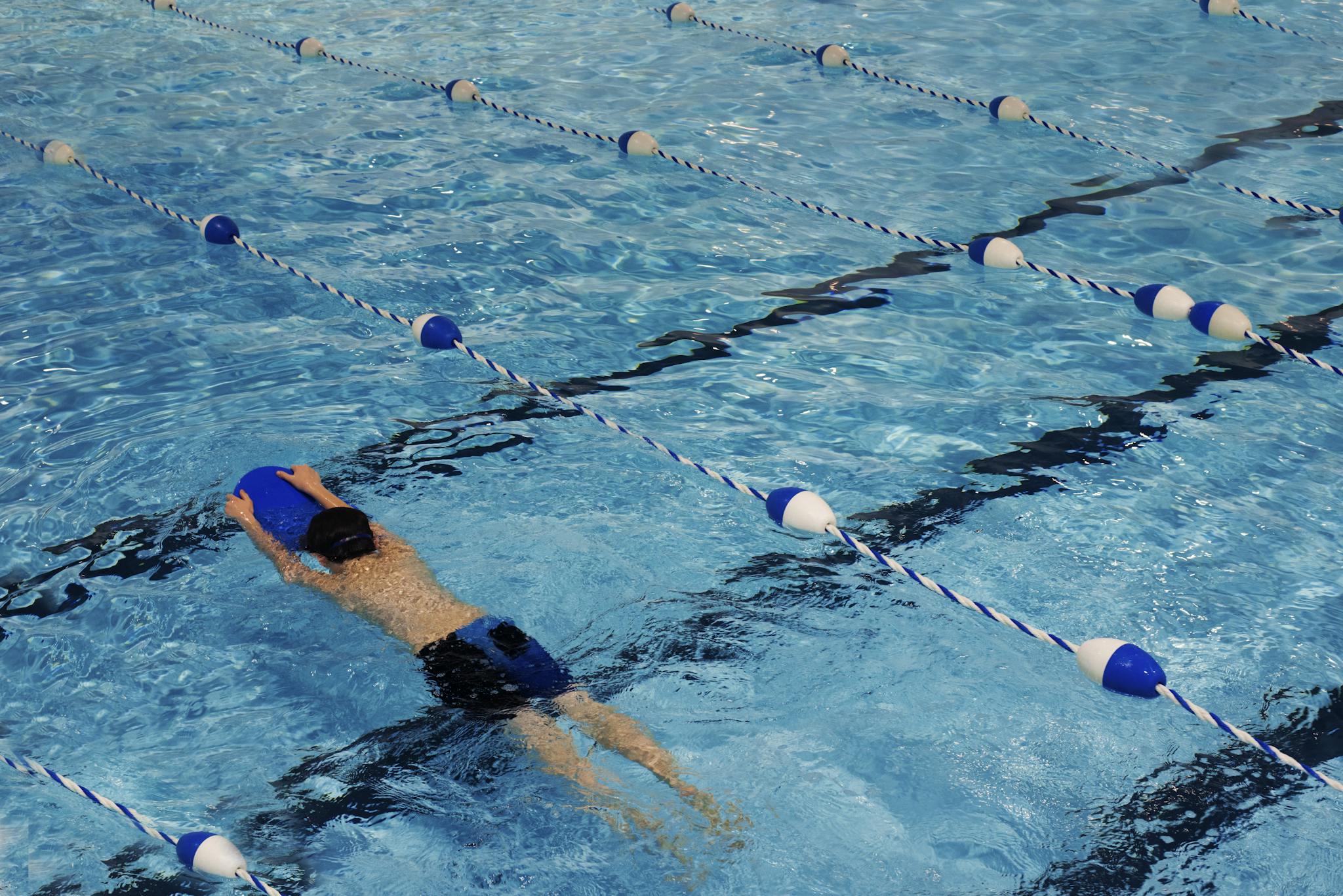 A young swimmer practicing with a kickboard in a swimming pool on a sunny day.