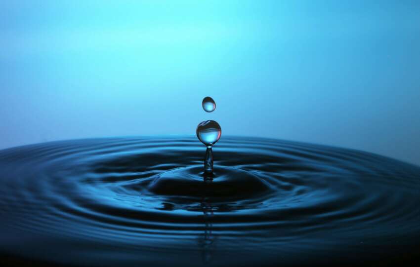 Macro shot of a perfect water droplet splash creating ripples on a blue background.