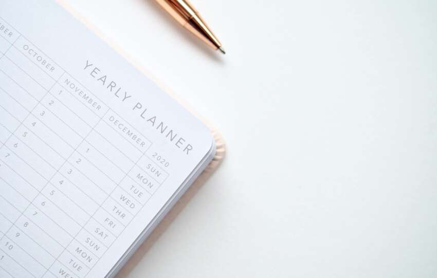 A stylish yearly planner open to a 2020 calendar page, accompanied by a golden pen on a clean white surface.
