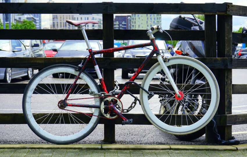 A vibrant bicycle locked to a wooden railing in a city parking lot with background cars.