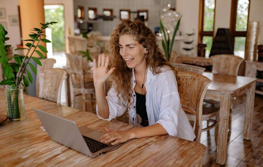 Smiling woman having a video call in a home-like setting with laptop.