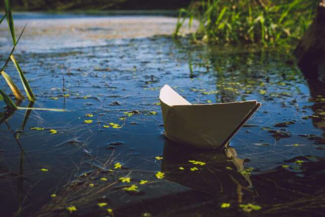 A serene paper boat softly floats on a calm lake, surrounded by nature.