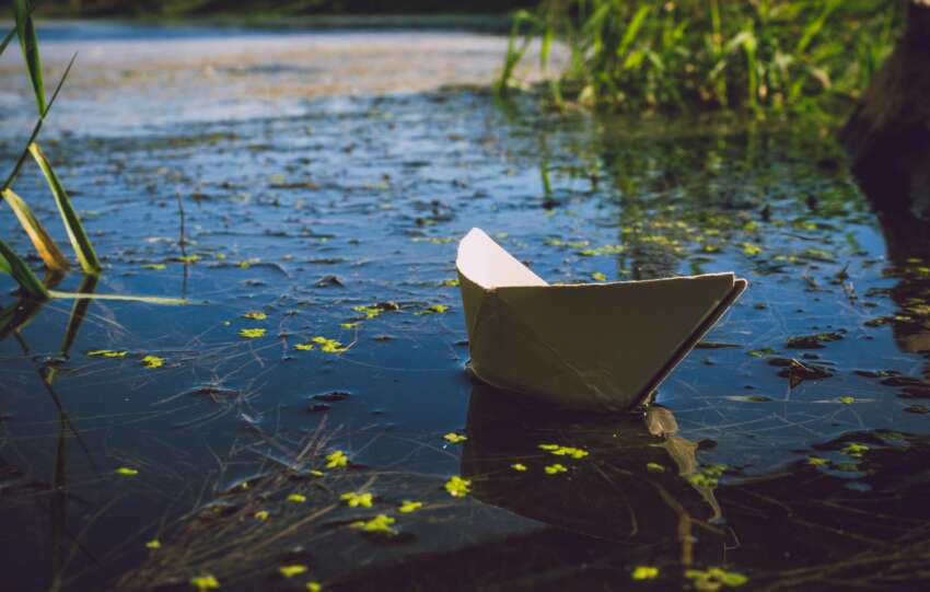 A serene paper boat softly floats on a calm lake, surrounded by nature.