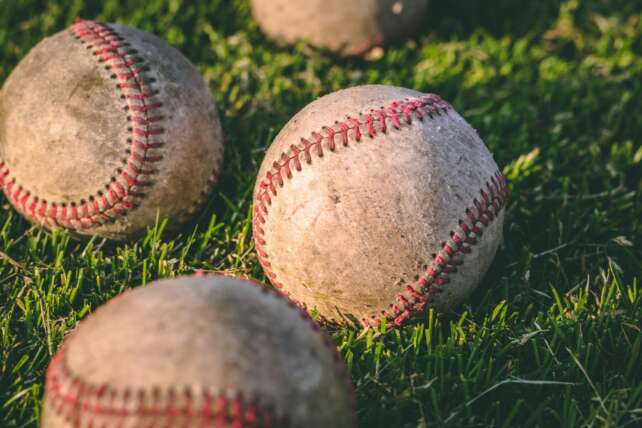Close-up of multiple baseballs lying on a grassy field in bright sunlight.