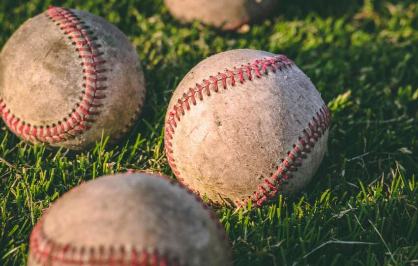 Close-up of multiple baseballs lying on a grassy field in bright sunlight.