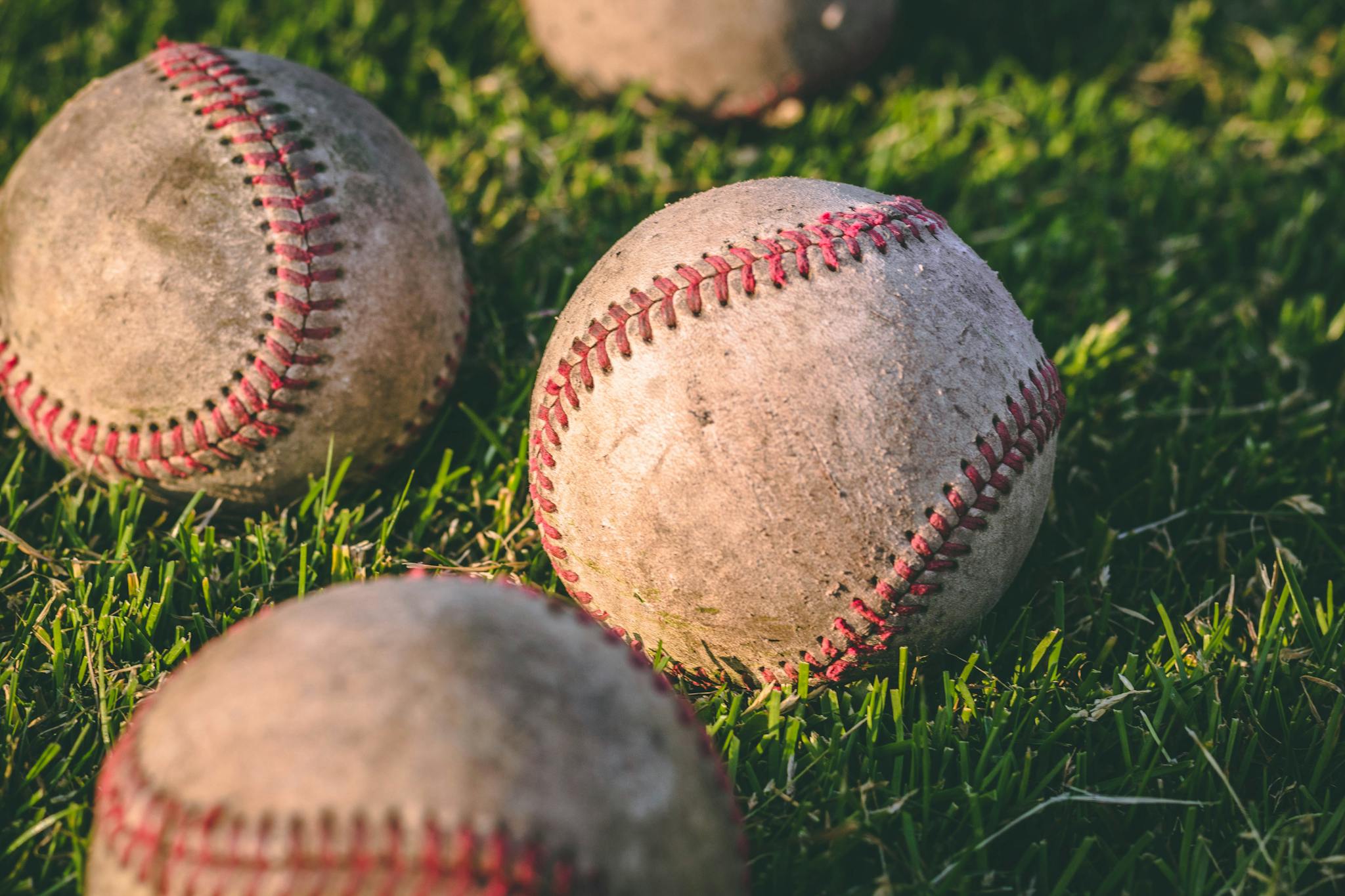 Close-up of multiple baseballs lying on a grassy field in bright sunlight.