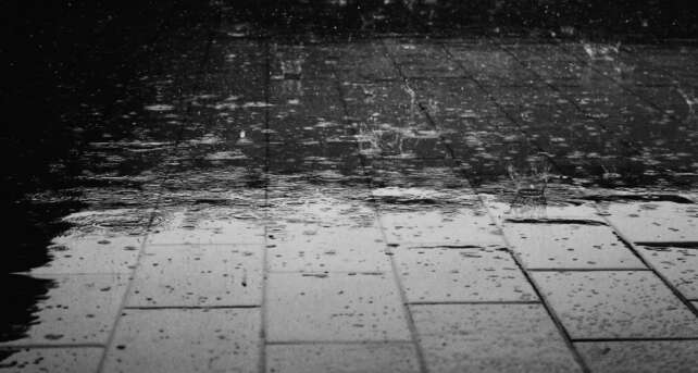 Monochrome image of raindrops creating splashes on a wet paved surface.