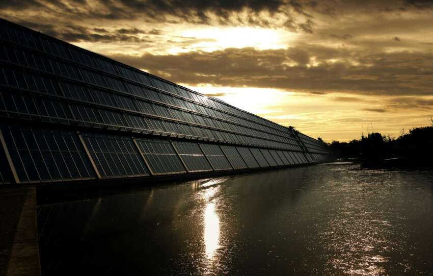Silhouetted solar panels reflect sunset in tranquil waters, showcasing renewable energy.