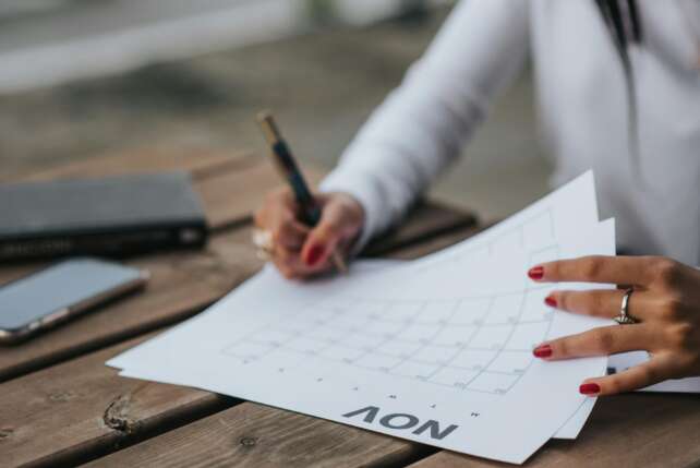 A woman planning with a calendar outdoors, jotting down notes on a wooden table with a pen.