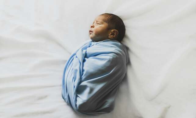A serene newborn baby wrapped in a blue blanket, sleeping peacefully indoors.
