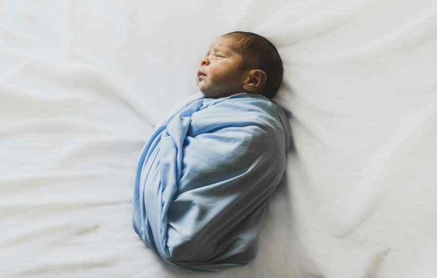 A serene newborn baby wrapped in a blue blanket, sleeping peacefully indoors.