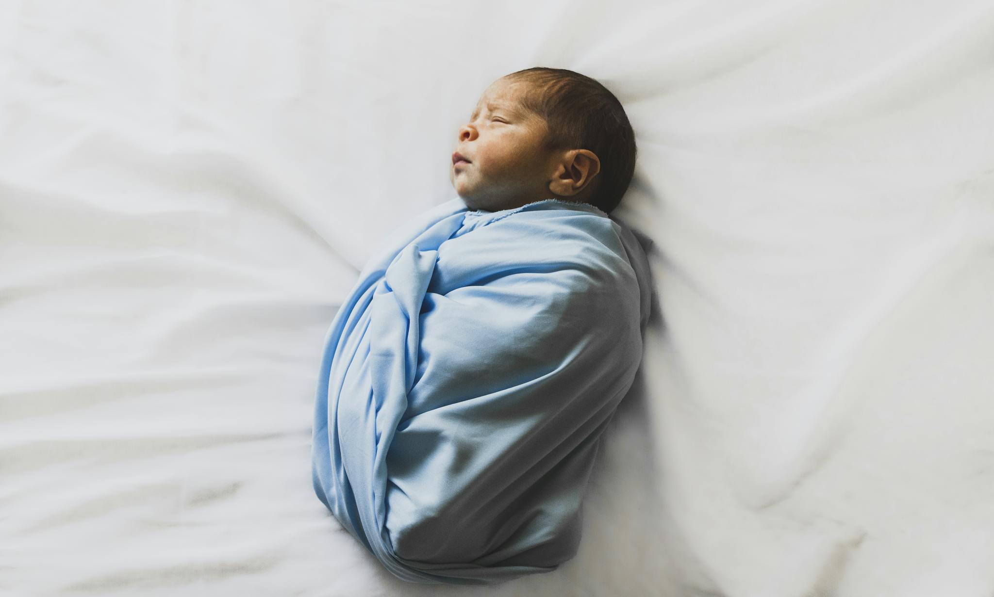 A serene newborn baby wrapped in a blue blanket, sleeping peacefully indoors.
