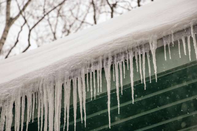Winter scene of icicles hanging from a rooftop after heavy snowfall.
