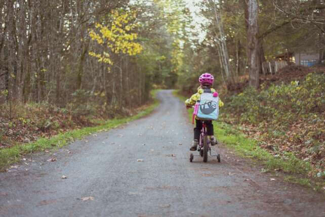 A young girl riding a bike with training wheels on a rural path surrounded by fall foliage.