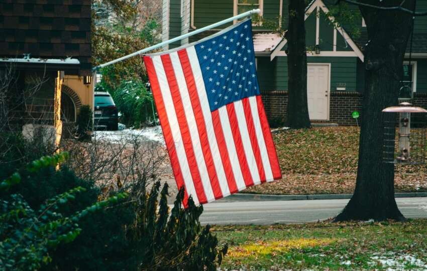 American flag flying proudly in a peaceful suburban neighborhood street.
