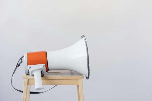 Close-up of a megaphone resting on a wooden chair with a minimalist background.