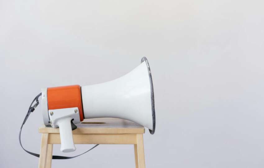 Close-up of a megaphone resting on a wooden chair with a minimalist background.