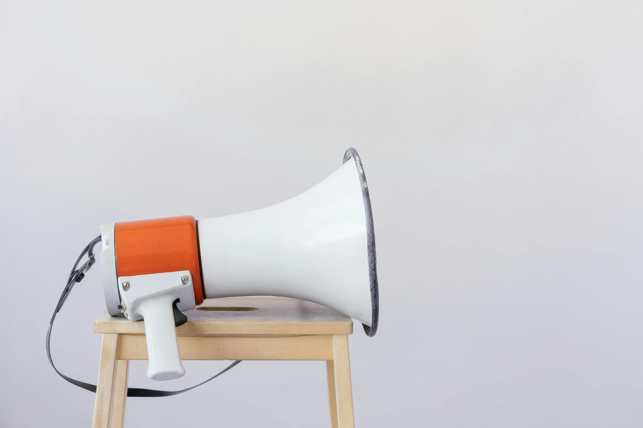 Close-up of a megaphone resting on a wooden chair with a minimalist background.