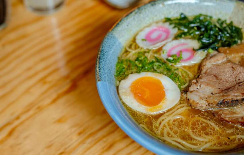 Close-up of a savory Japanese ramen bowl featuring noodles, egg, and toppings on a wooden table.