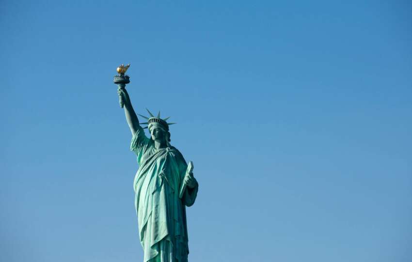 Iconic Statue of Liberty with torch against a bright blue sky, symbolizing freedom.