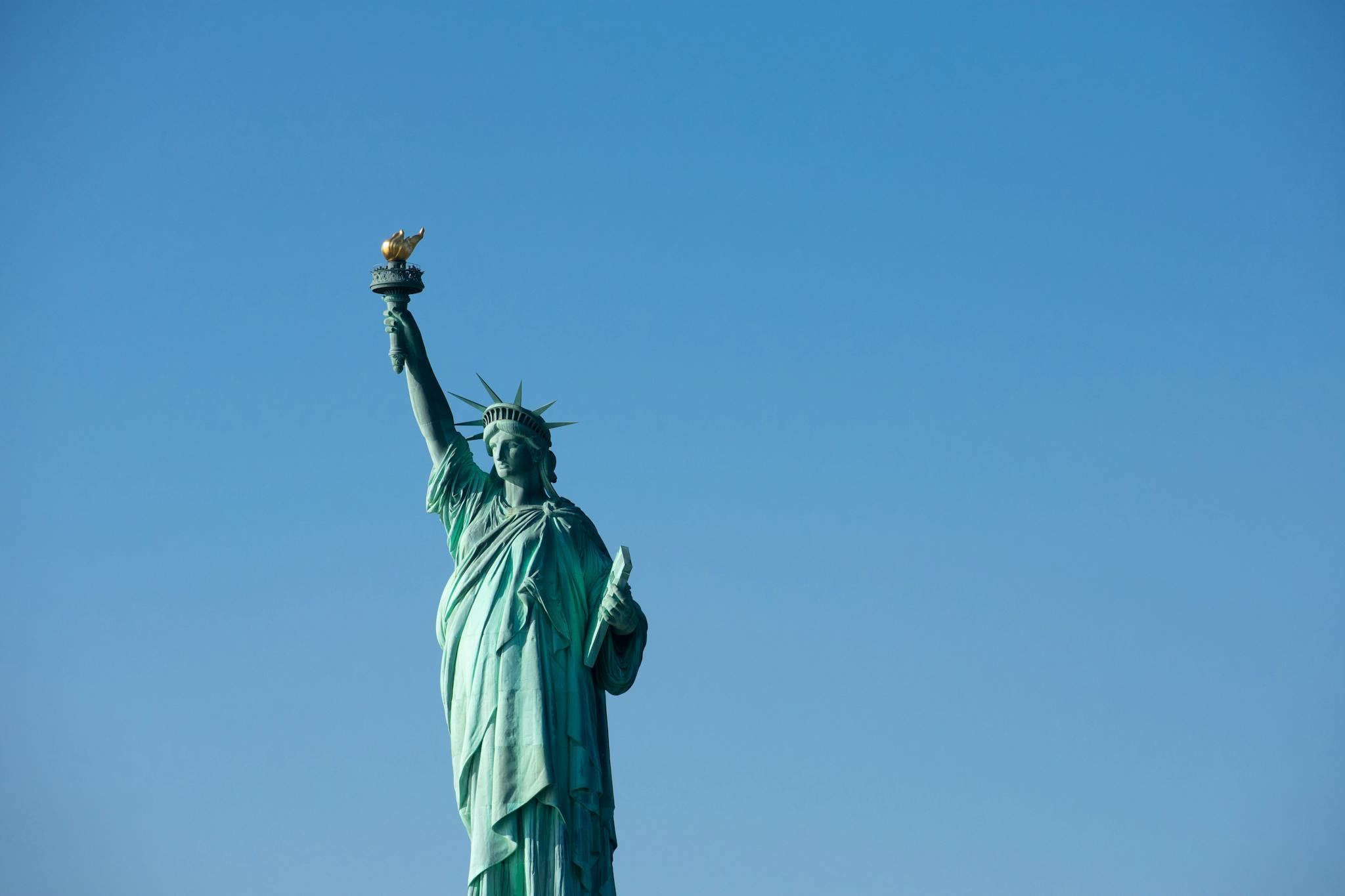 Iconic Statue of Liberty with torch against a bright blue sky, symbolizing freedom.