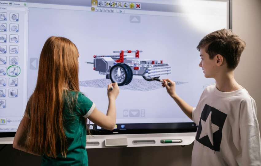 A boy and girl collaborate on a robotics project using a digital screen in a classroom setting.