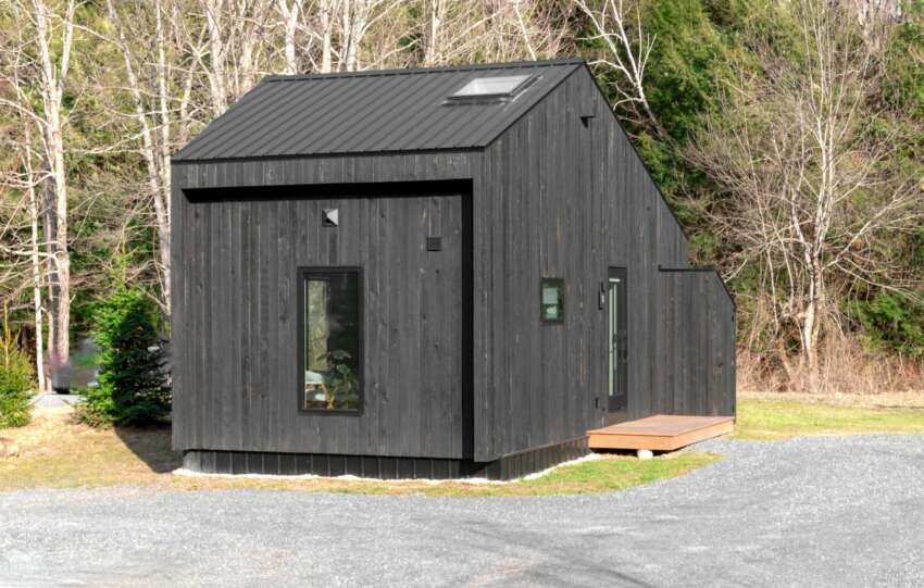A minimalistic black tiny house nestled in a forest area, showcasing sustainable living.