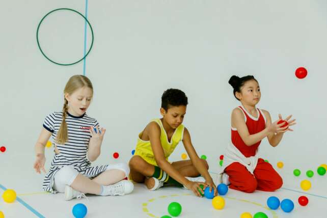 Three children of diverse backgrounds playing with colorful balls indoors, enjoying fun and creativity.