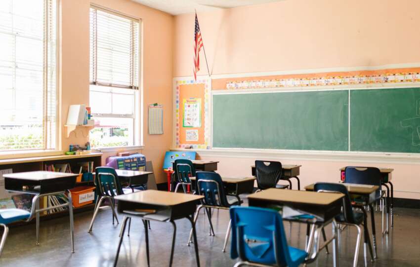 An inviting, sunlit classroom with empty desks and an American flag, ready for students.