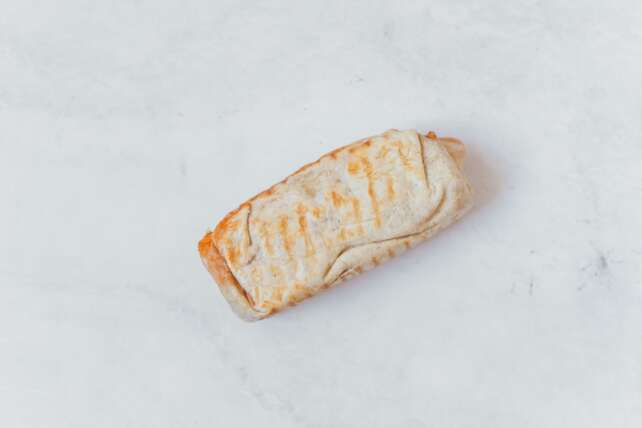 A minimalist flat lay of a wrapped burrito on a clean white surface, showcasing Mexican cuisine.