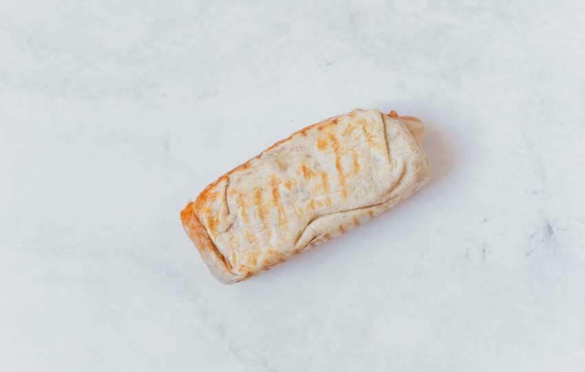 A minimalist flat lay of a wrapped burrito on a clean white surface, showcasing Mexican cuisine.