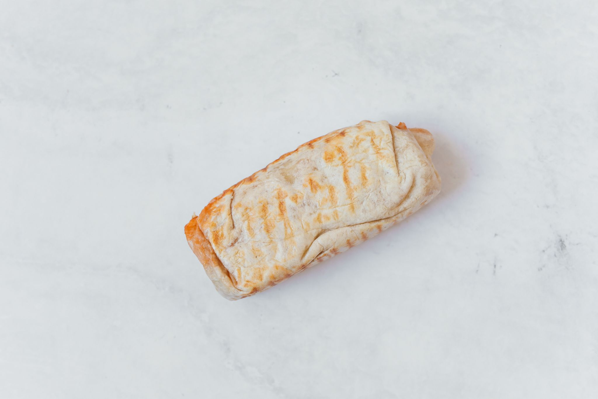 A minimalist flat lay of a wrapped burrito on a clean white surface, showcasing Mexican cuisine.