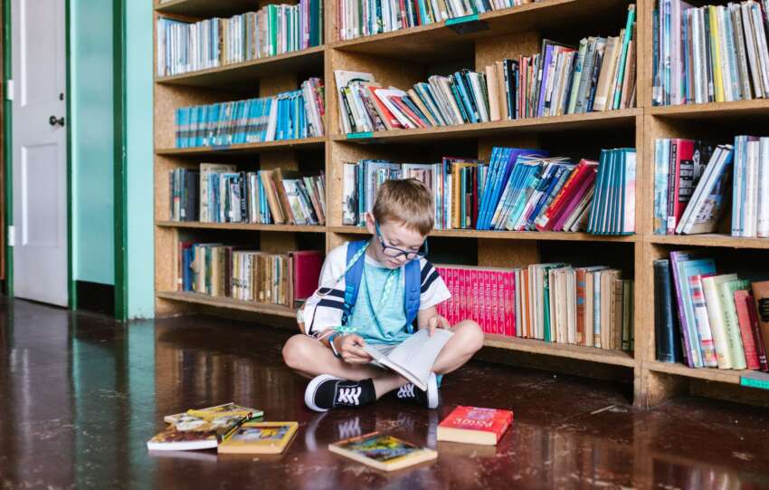A young boy engrossed in a book, sitting by bookshelves in a library, capturing the essence of learning.