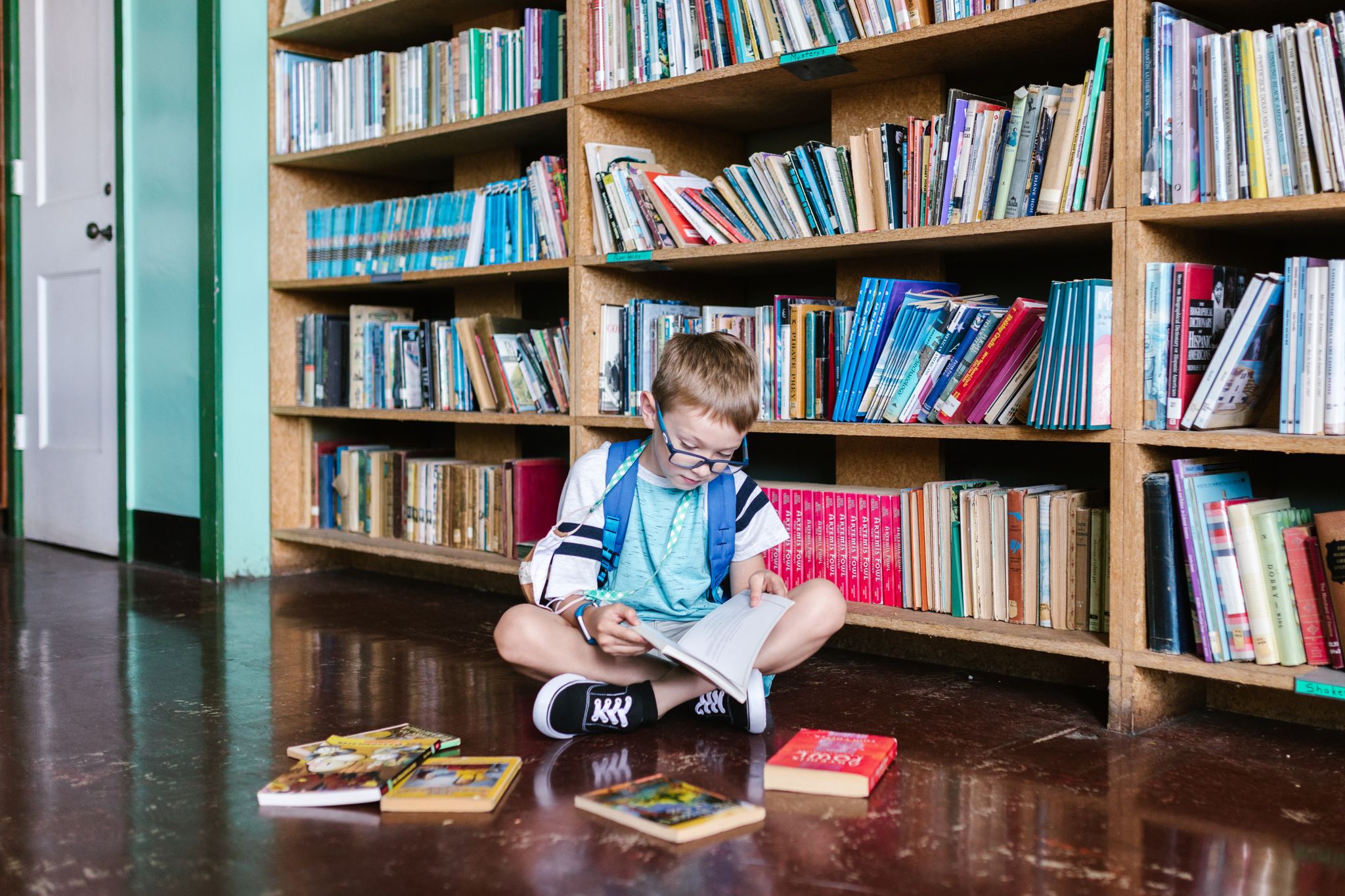A young boy engrossed in a book, sitting by bookshelves in a library, capturing the essence of learning.