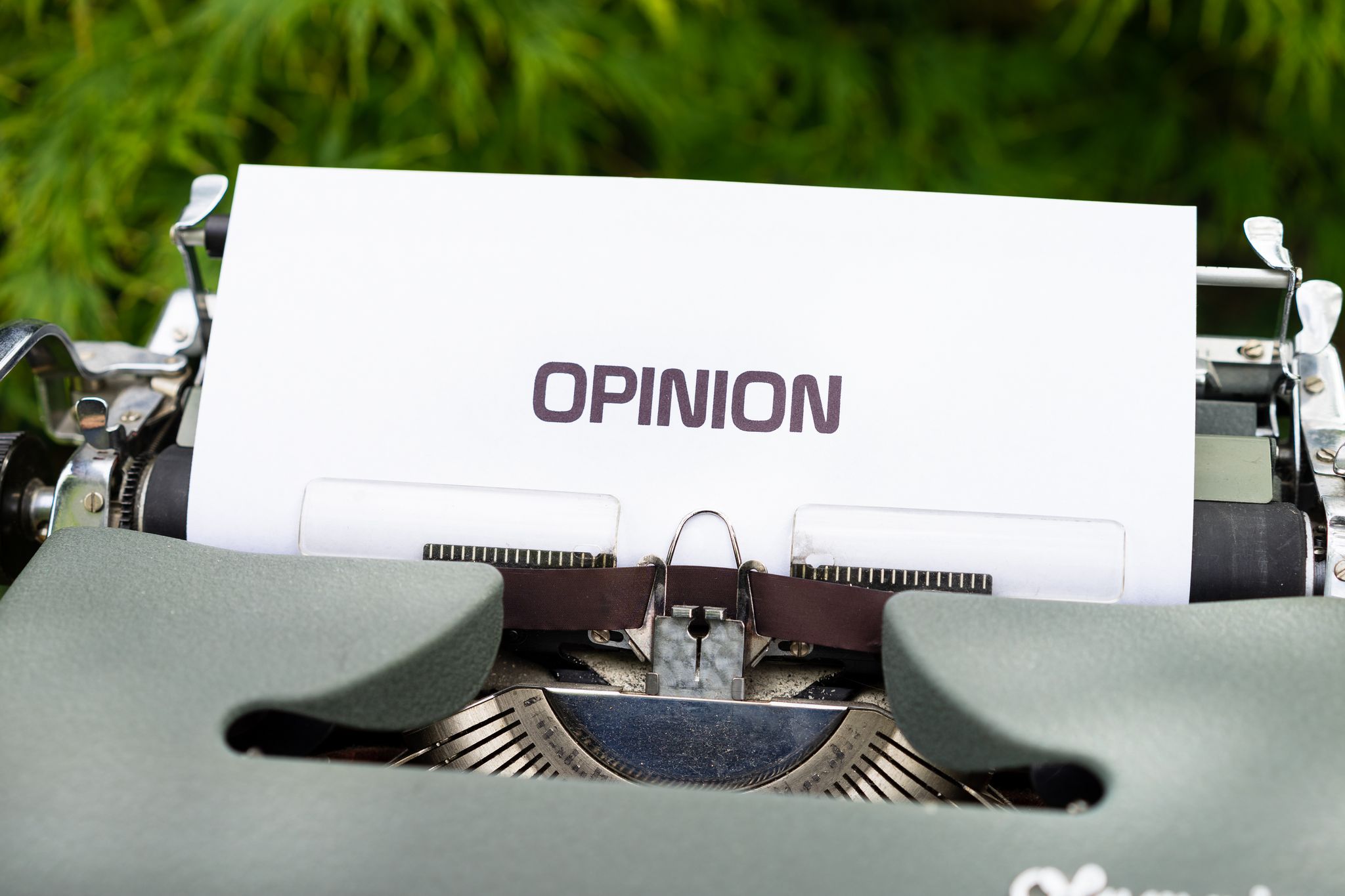Close-up of a typewriter with paper showing the word 'Opinion' outdoors.