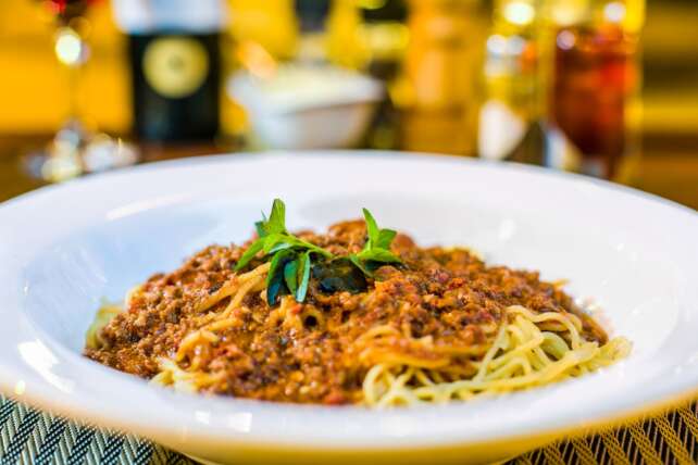 A close-up of spaghetti Bolognese topped with fresh basil in a restaurant setting.