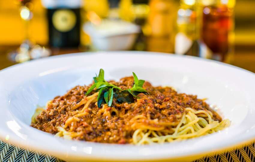 A close-up of spaghetti Bolognese topped with fresh basil in a restaurant setting.