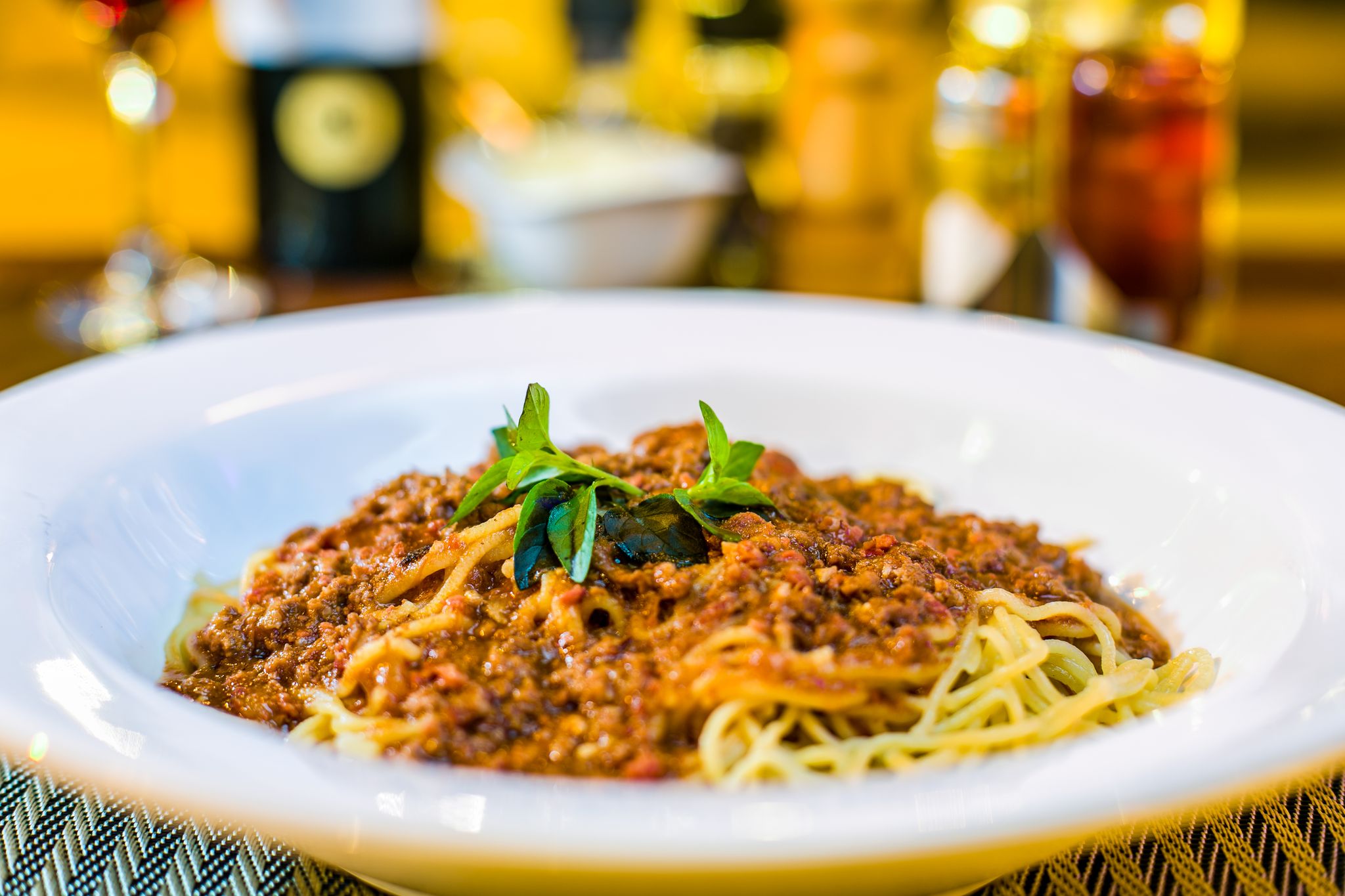 A close-up of spaghetti Bolognese topped with fresh basil in a restaurant setting.