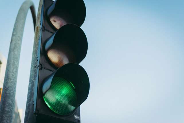 Close-up of a green traffic light against a clear blue sky, symbolizing go and safety.